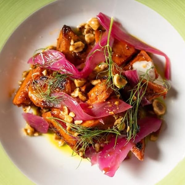 Roasted carrots with pickled red onions, chopped nuts, and fresh dill on a white plate.
