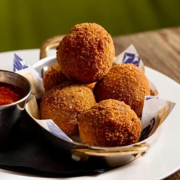 Fanny's Italian arancini, golden-brown fried rice balls, served in a basket with a side of red sauce.