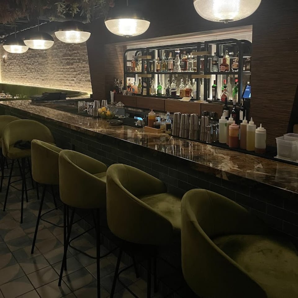 Fanny's dimly lit bar with olive green velvet stools, a marble counter, and a well-stocked liquor shelf.