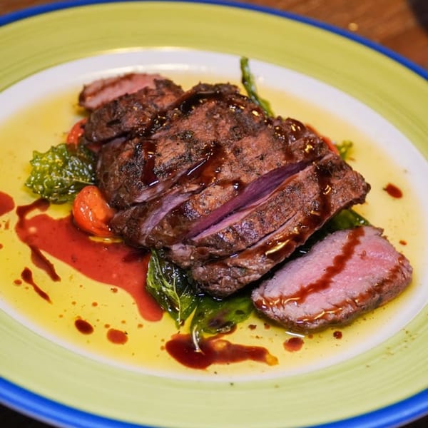 Sliced steak with a dark glaze, green vegetables, and red sauce on a yellow and green plate.