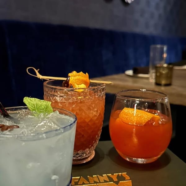 Three vibrant cocktails, garnished with mint and orange, on a Fanny's branded coaster.